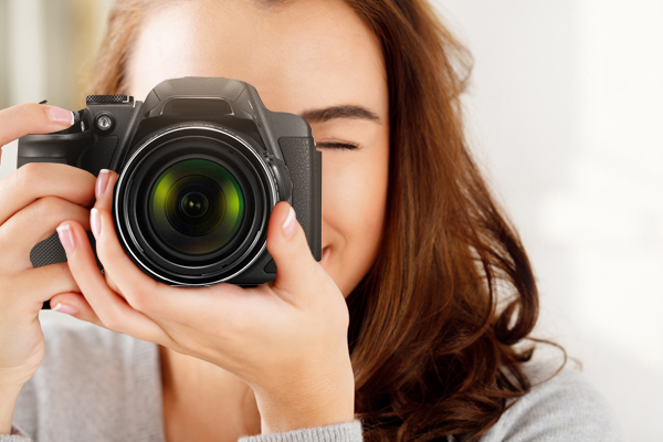 mulher sorridente apontando uma máquina fotografica para o leitor