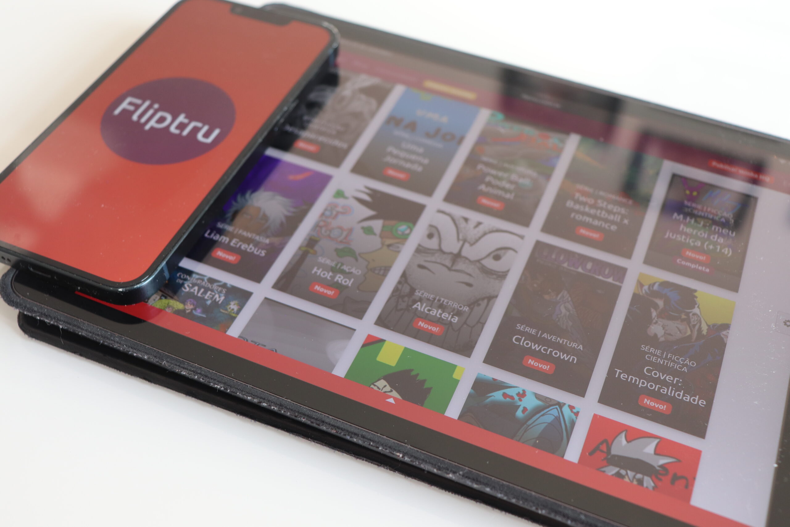 celular com logo da empresa em cima de tablet com capas da revistas em quadrinhos