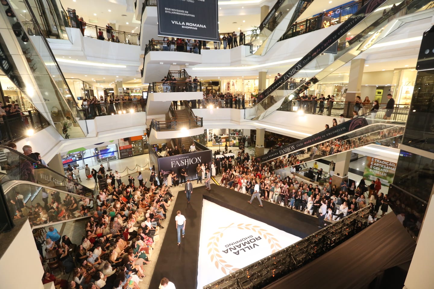 pessoas reunidas ao redor da passarela do desfile no shopping villa romana em foto aerea